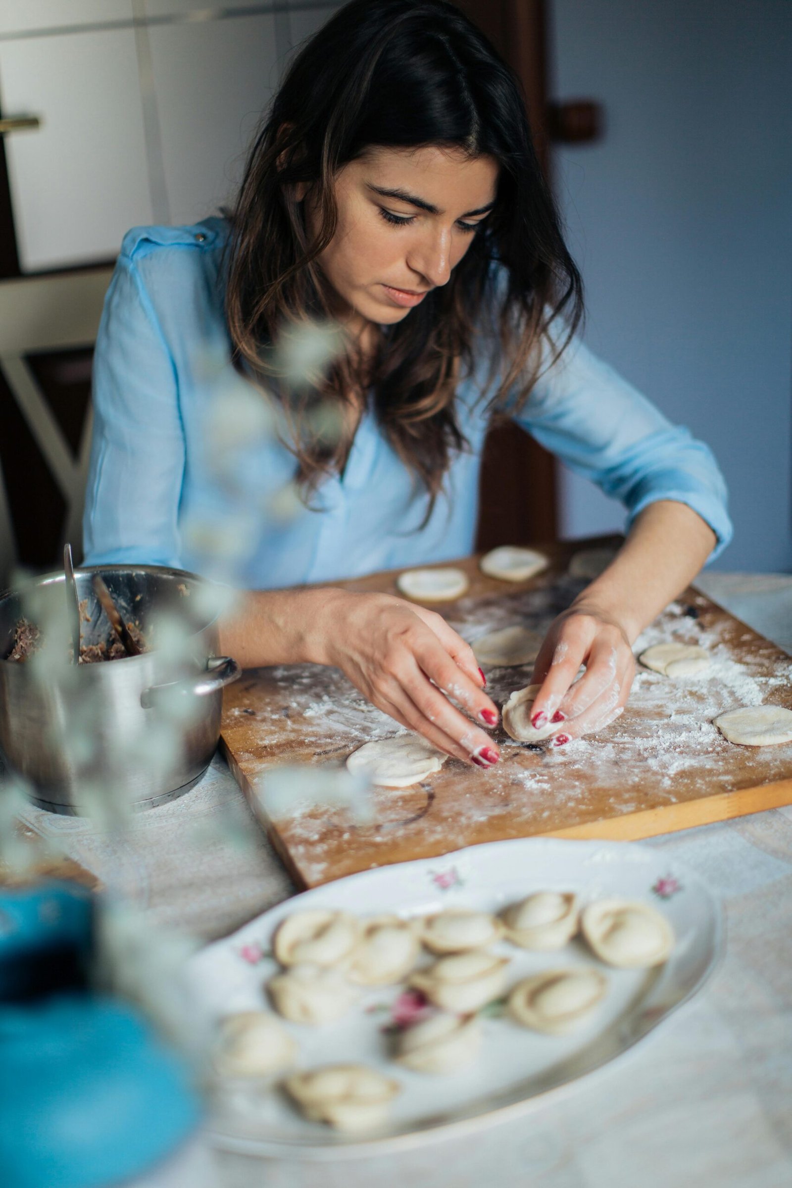 pexels-photo-3893669-3893669 A woman carefully prepares homemade pastries on a wooden board in a cozy kitchen setting.